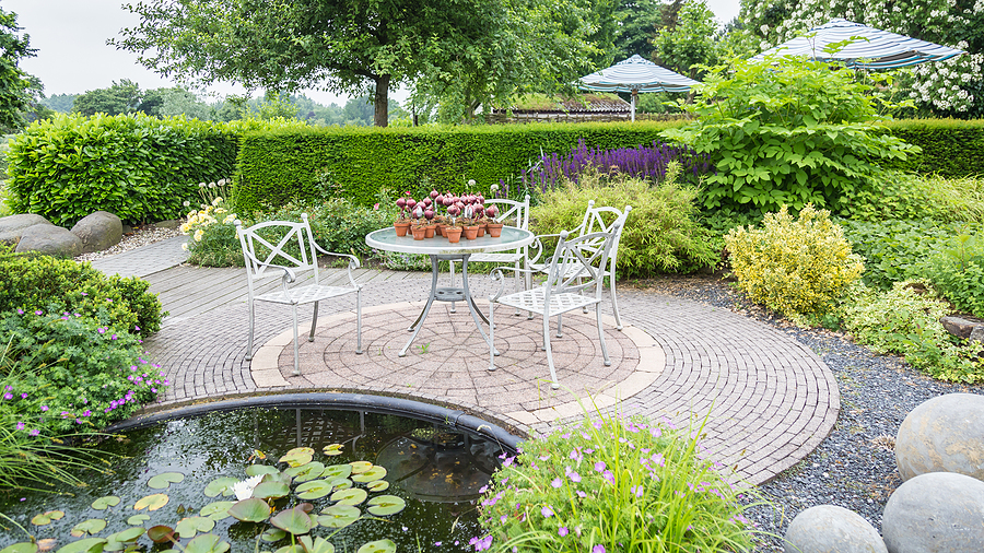 Garden With Pond And Classic White Chairs And Table On A Patio