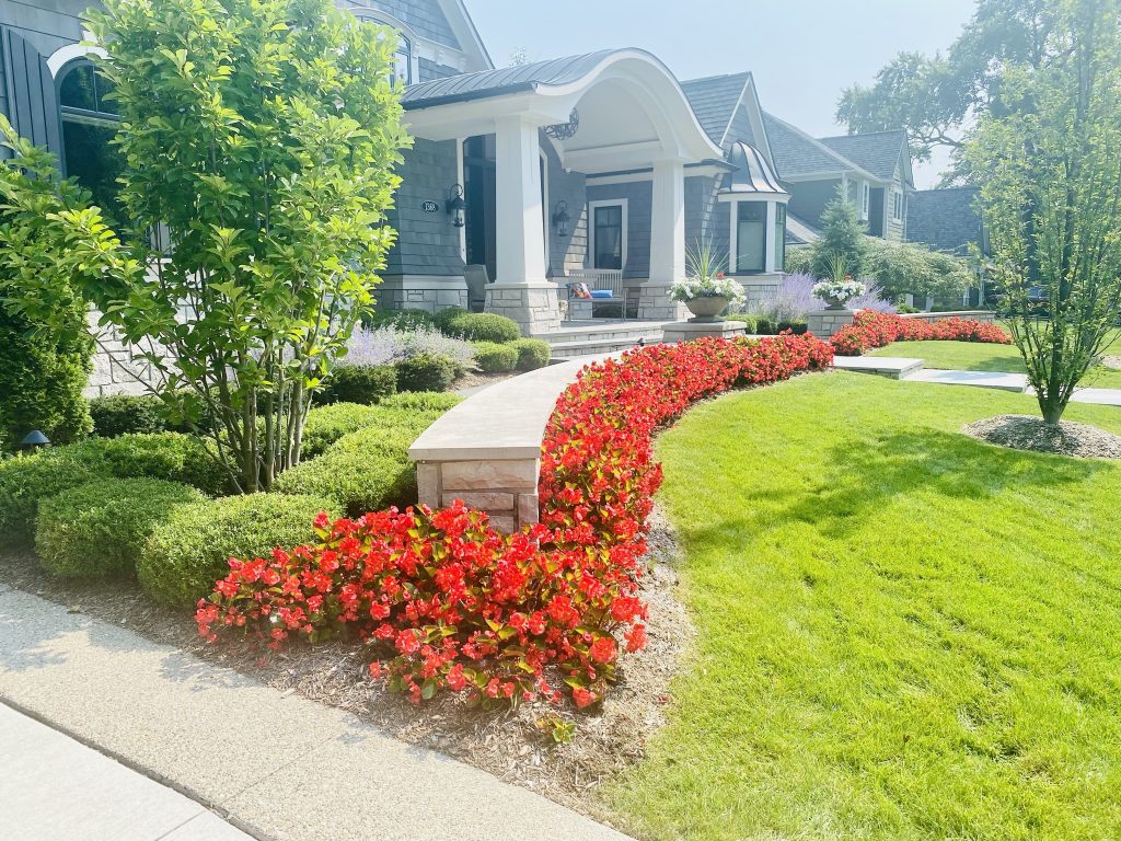 Beautifully landscaped front yard with short stone wall dividing the flower beds from the lawn.