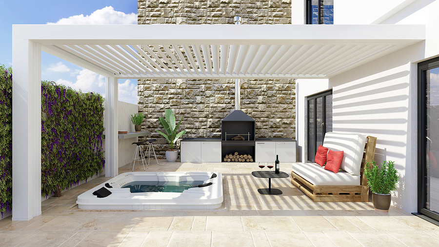 Modern urban patio with white bio climatic pergola and whirlpool. Barbecue and white pallet couch next to hot whirlpool bath.