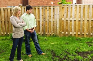Young couple standing in their backyard looking concerned over landscaping issues. 