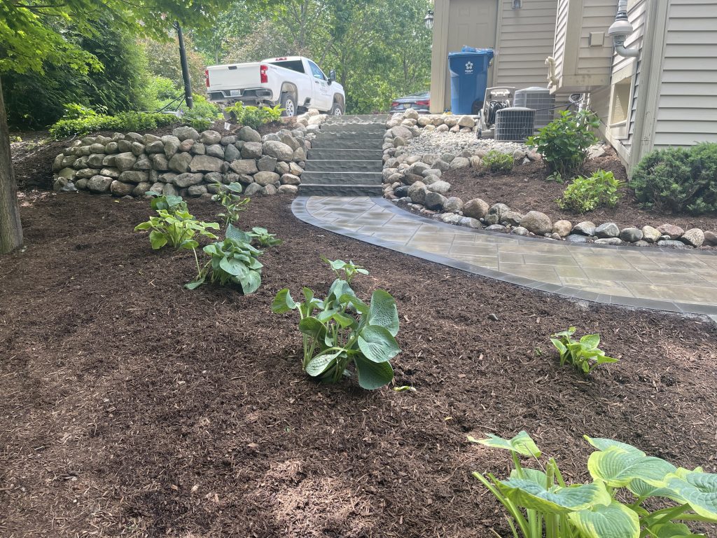 landscaping surrounds a stone large boulder retaining wall with brick paver walkway
